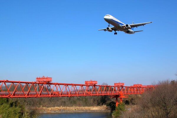 Passagierflugzeug fliegt über rote Brücke