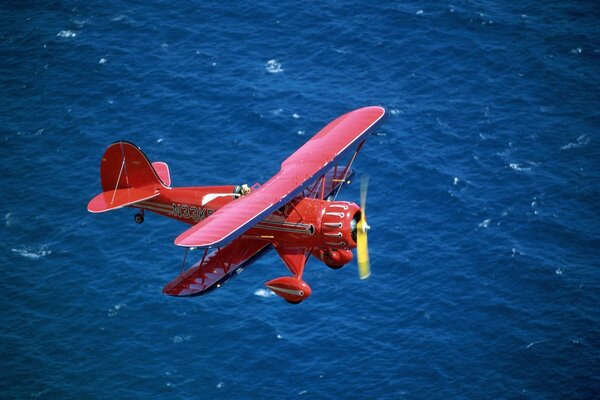 Biplan rouge vole au-dessus de la mer