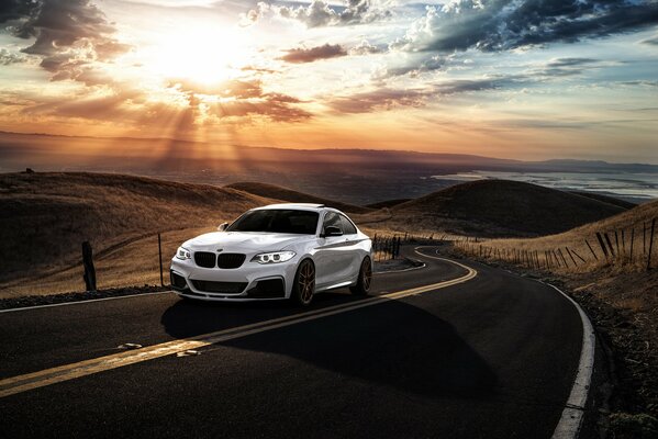 Un BMW blanco corre por la carretera de montaña de San José, lejos de una puesta de sol escénica