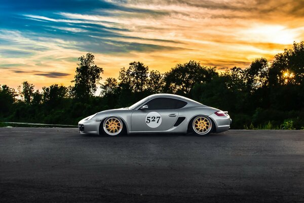 Silberner porshe Cayman bei Sonnenuntergang