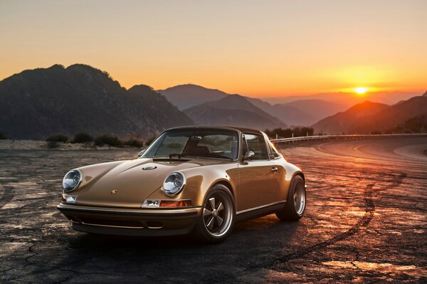 Porsche 911 is standing on the side of the road in the sunset