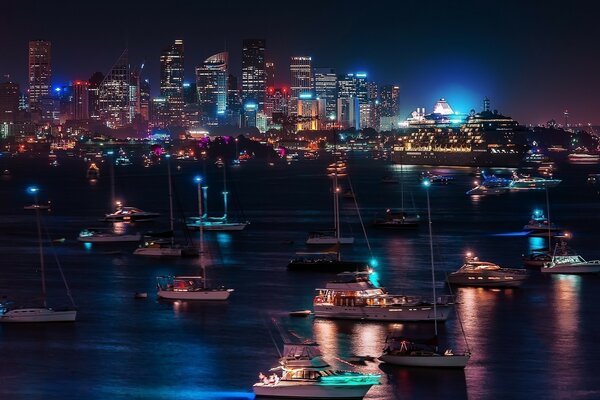 Blick auf die Nachtstadt vom Ufer des Flusses, auf dem viele Yachten liegen