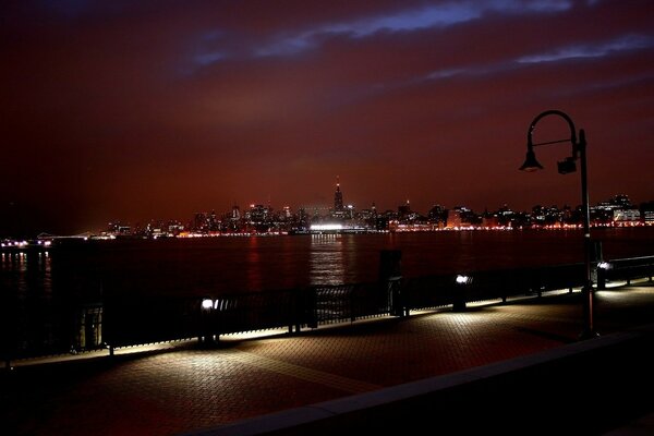 Dim lighting in a New York city on the banks of the river there are benches