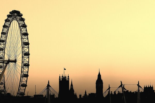 Sylwetki London Eye i Big Bena na żółtym niebie