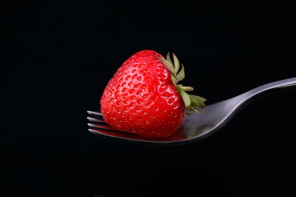 Fraises rouges sur une fourchette sur fond noir