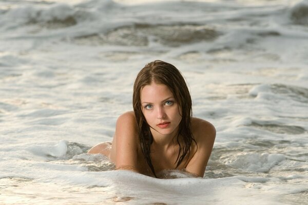 A girl with wet hair poses in sea foam