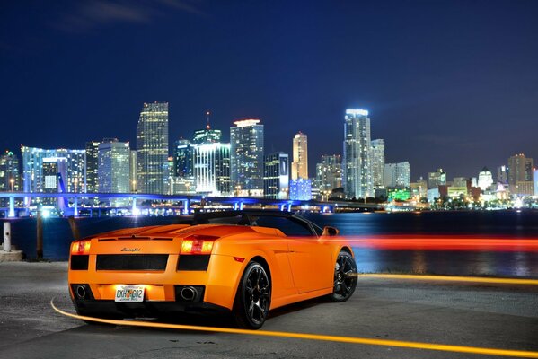 Pomarańczowy supersamochód na tle panoramy nocnego miasta
