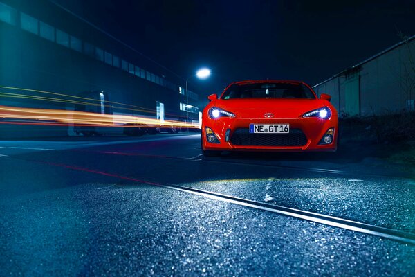 A red car on the road by a concrete fence