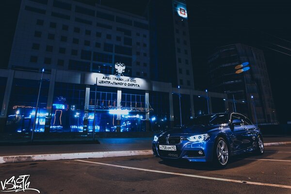 Blaues Auto auf dem Hintergrund des blauen Nachtgebäudes
