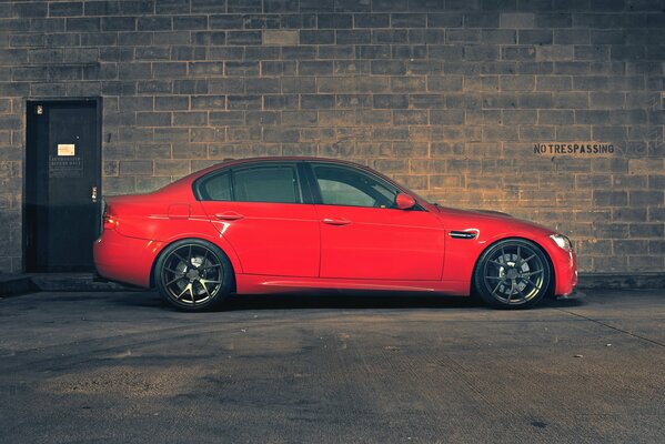 BMW rouge se dresse dans le profil sur fond de mur de briques