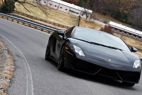 A black Lamborghini rides on a road with bumpers on the edges against the background of an autumn rustic landscape