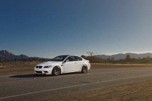 A white BMW is driving on the road against the backdrop of snowy mountains