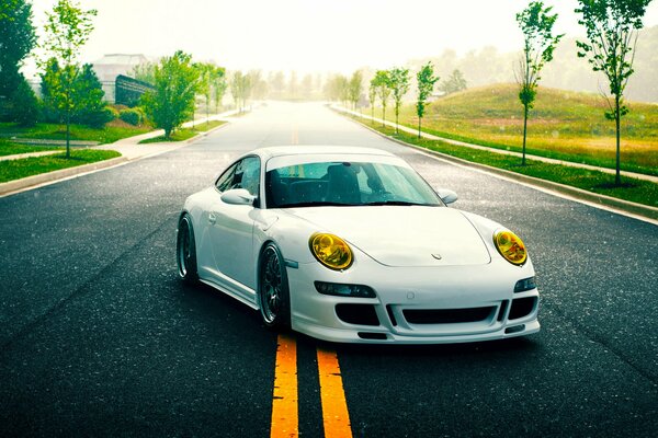 Porsche bianca con fari gialli sulla linea di demarcazione gialla dell autostrada tra i verdi luminosi