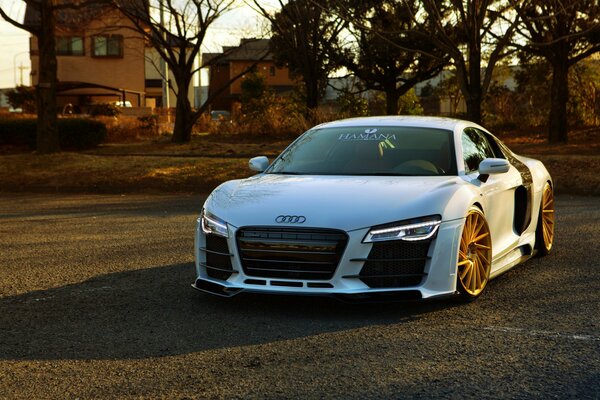 White Audi r8 with orange wheels and headlights on , standing on the road