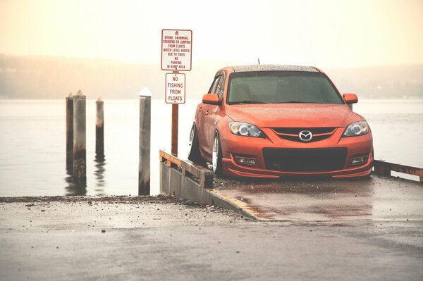 Mazda de color naranja junto al mar