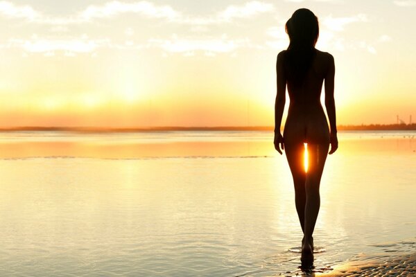 Silueta de una mujer desnuda en el fondo del sol Poniente. Playa