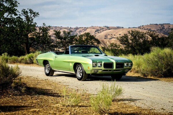 A pale green Pontiac convertible standing on the road against a background of trees and hills