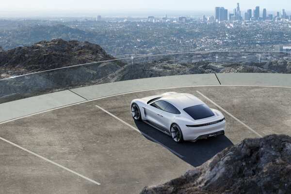 Biały Porsche stojący na tarasie widokowym z widokiem na metropolię