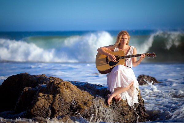 A girl with a guitar on a rock on the seashore