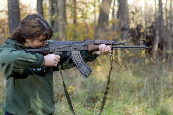 Mujer con fusil AK-47 disparando en el bosque
