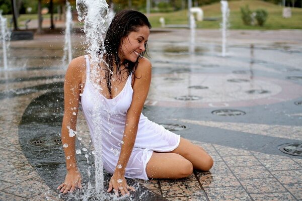 Dziewczyna w białej sukience kąpie się w fontannie