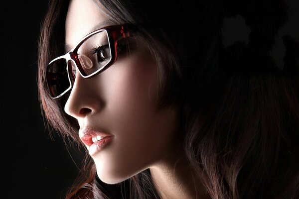 Ragazza asiatica con gli occhiali su sfondo nero