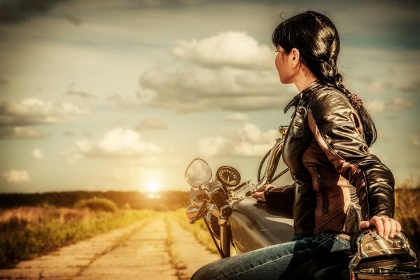 Una ragazza su una moto cavalca verso il tramonto