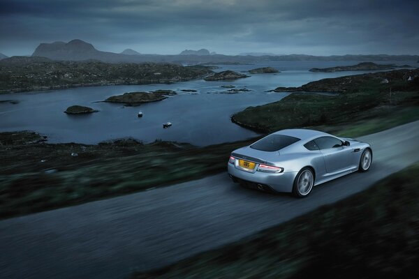 A gray car is driving on an evening road