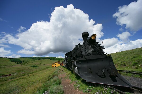 Locomotora negra contra un cielo azul con nubes