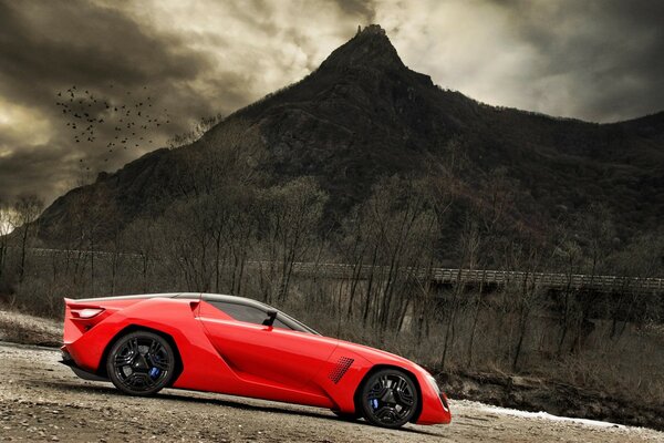 A red concept car stands on gravel against the backdrop of a gloomy mountain