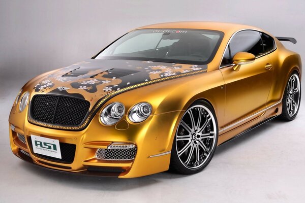 A gold-colored tuned Bentley with graffiti on the hood