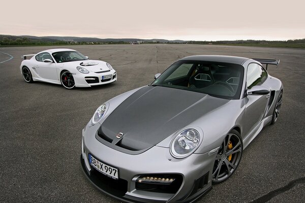 Two cool cars at the airfield. One is white, the other is gray