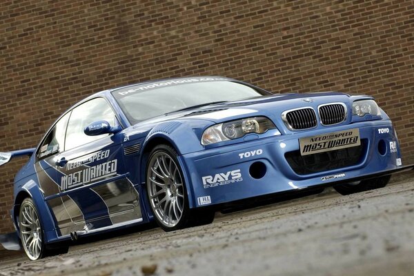 A blue bmw is standing on the road near a brick wall