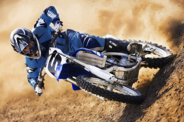 Motociclista con traje azul y casco corre por la arena