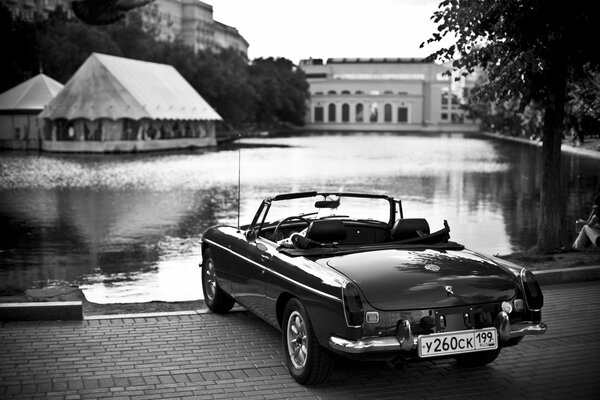 Foto retro con un convertible junto al agua y casas en el fondo