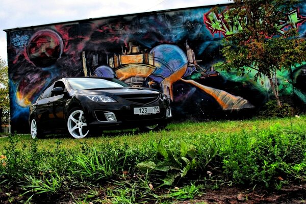 Black mazda on the background of graffiti and a small tree