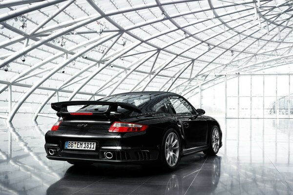 A black Porsche 911 in a transparent futuristic hangar