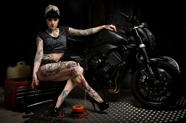 Fille avec des tatouages assis près d une moto noire