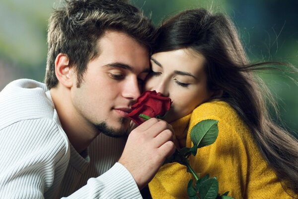 Das Mädchen und der Kerl atmen den Duft einer roten Rose ein