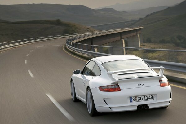 Porsche blanc 911 Gee TI 3 sur la piste en mouvement sur fond de paysage de montagne