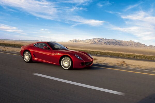 Un ferrari rojo corre por la carretera en medio de una montaña y un cielo azul