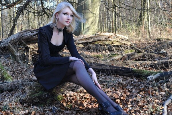 Blonde girl in a black dress on a background of trees