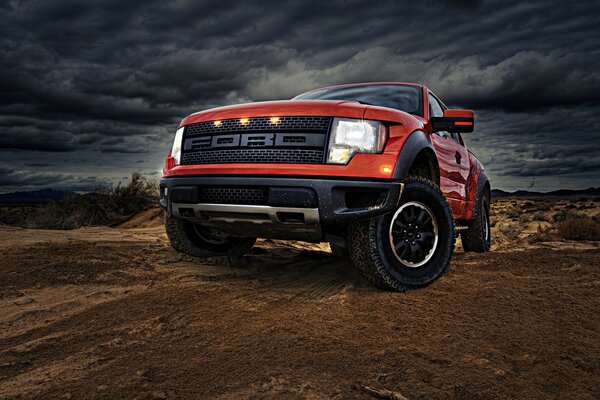 Coche Ford rojo en medio de la arena y las nubes