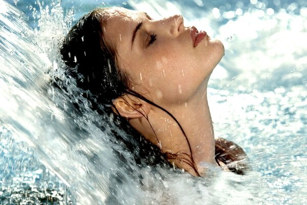 A girl with her eyes closed under a stream of water