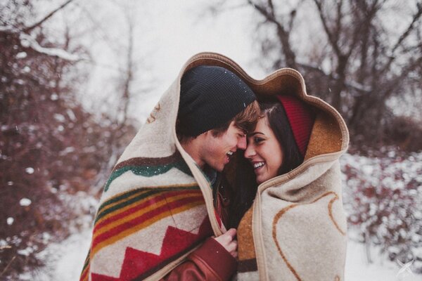 A couple in a blanket rolled up hugging in winter