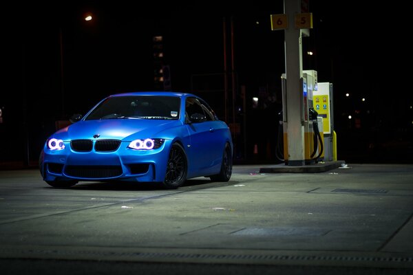 Niebieski samochód w nocy na stacji benzynowej