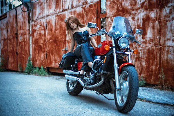 A girl is sitting on a motorcycle against a wall