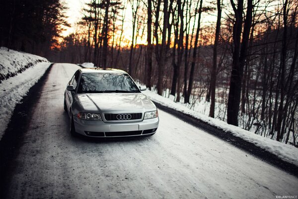Zachód. białe Audi A4 na zaśnieżonej leśnej drodze