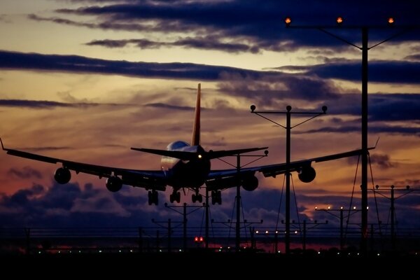 The plane lands on the runway against the backdrop of a beautiful sunset