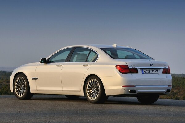 A white BMW sedan is driving on an asphalt road